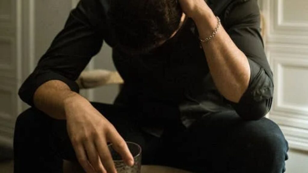 Yoga for Addiction Recovery: How Mind-Body Practices Promote Long-Term Sobriety 2 Man looking down, holding a drink, appearing lonely and dejected.