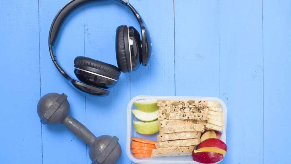 The Role of Nutrition and Fitness in Addiction Recovery 2 Headphones sit on a table alongside a healthy selection of fruits, vegetables, and grains, set against a blue wall.