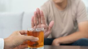 The hands of patients gently stop an offered hard liquor drink. The image is softly focused, showing only the hands.