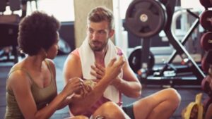 A man talks with his therapist and instructor in the midst of a busy gym.