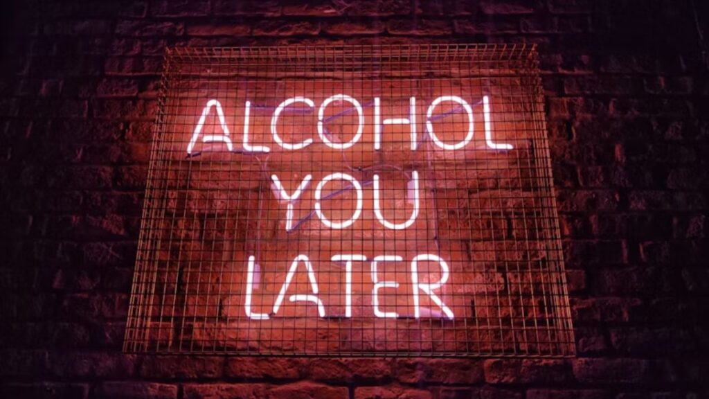 Alcohol Detox vs. Drug Detox: What’s the Difference? 3 A pink neon sign reading 'Alcohol You Later' illuminates a dimly lit nighttime street scene.