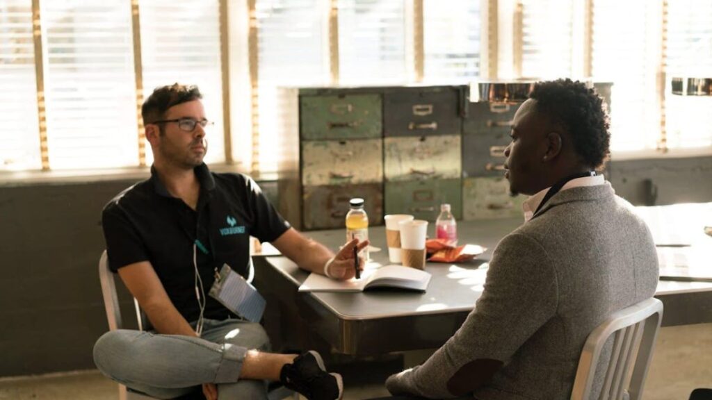 Alcohol Detox vs. Drug Detox: What’s the Difference? 4 A therapist in a blue shirt holding a notebook, providing therapy to a suited man, with some drinks on the table.