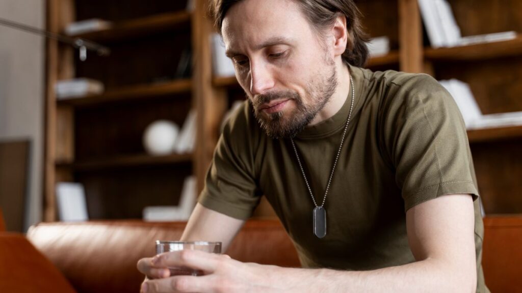 The Science of Addiction: Why It’s More Than Just “Willpower” 4 Science of addiction, a man sits on a sofa looking down at his drink, seemingly deep in thought.