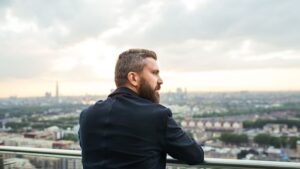 A man rests on a rooftop deck of a corporate skyscraper at sunset, surrounded by city buildings, reflecting on recovering without quitting his career.