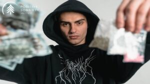A man in black hoddie holding cocaine and money