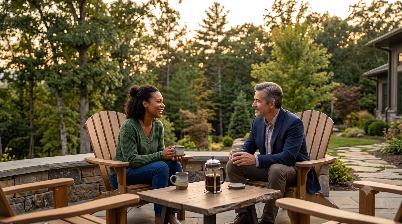 Two recovering individuals drinking coffee together on an outdoor patio surrounded by trees.